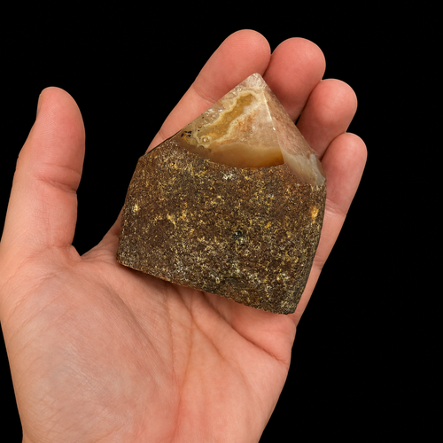 Hand-held front view of a unique honey brown semi-polished agate point with natural rough base and polished apex, shown for size reference on a black background.