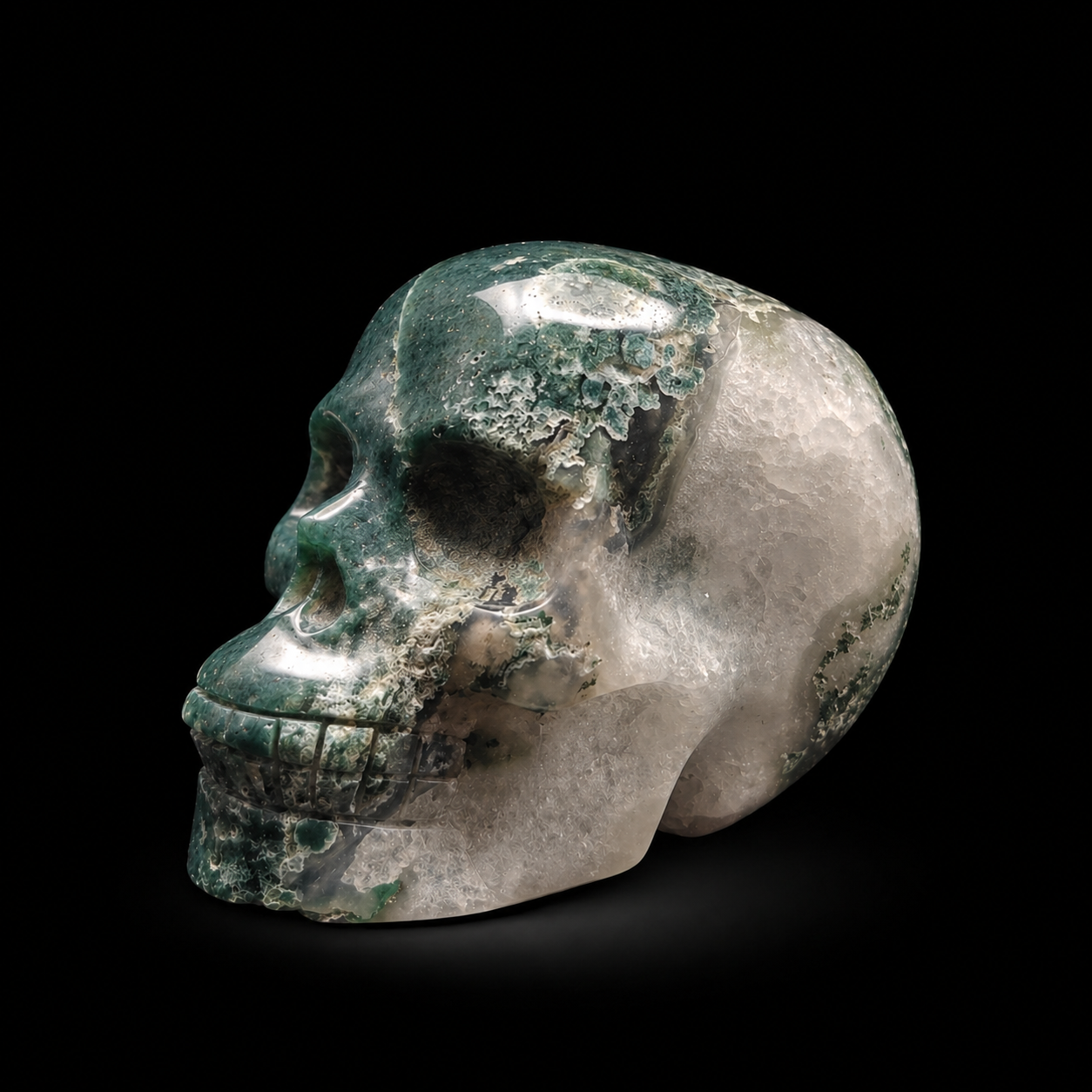 Moss agate skull angled side view showing polished green moss agate, white natural patterning and carved skull profile
