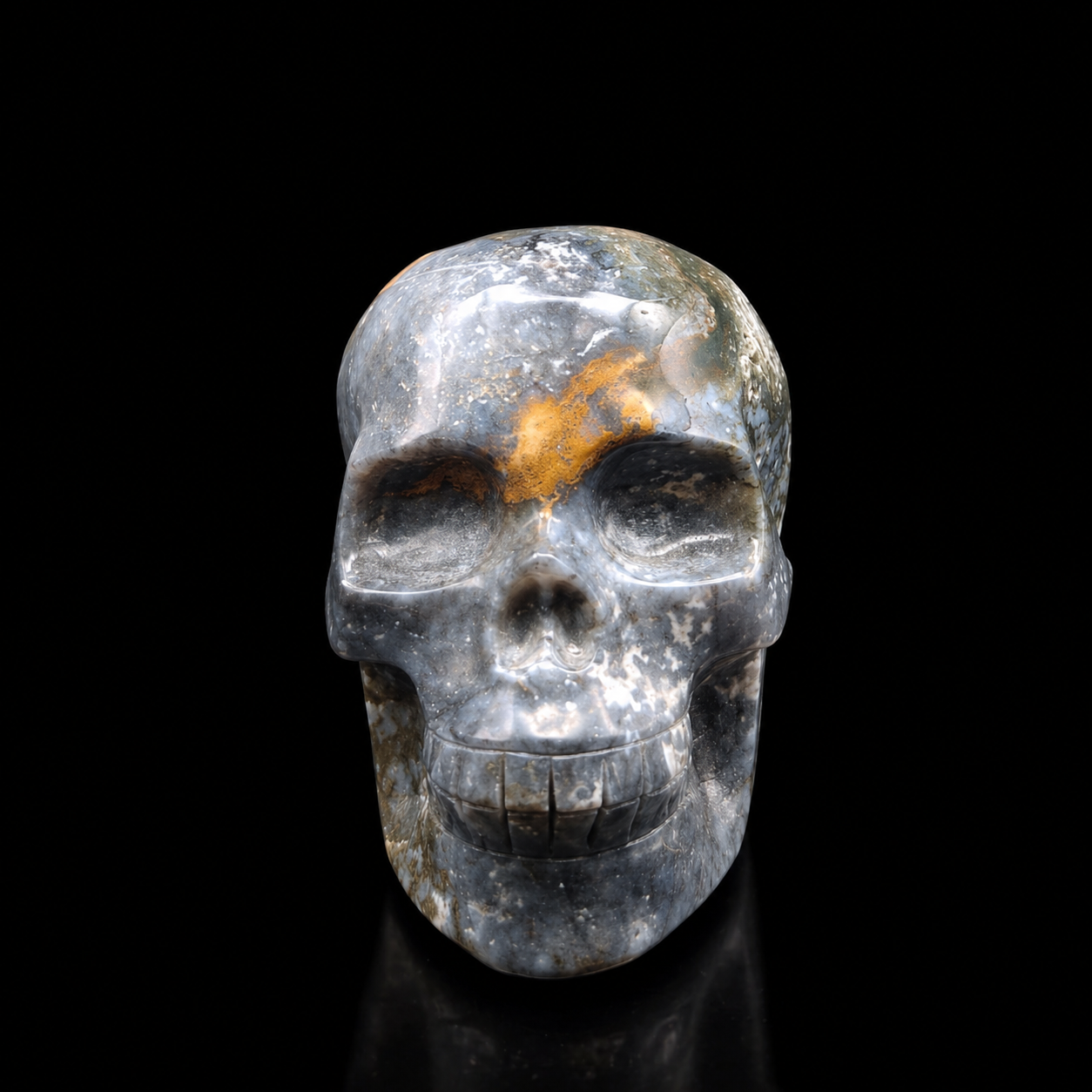Front view of a polished blue moss agate skull carving with grey-blue tones, golden markings and natural moss-like inclusions