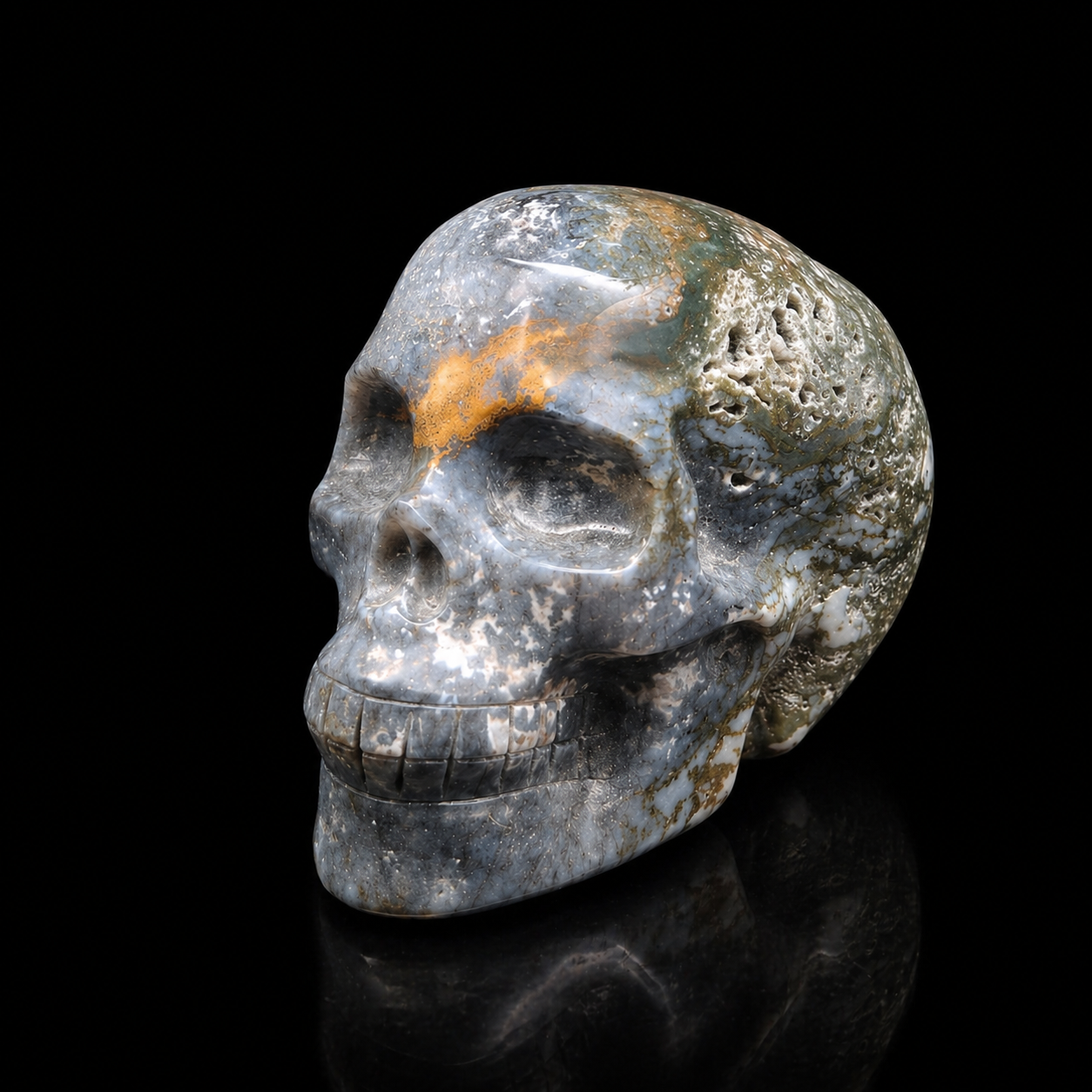 Opposite side view of a polished blue moss agate skull carving with natural moss inclusions, blue-grey tones and textured agate patterning