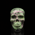 Ruby Zoisite skull front view, 630g polished green crystal carving with ruby-pink veining and dark speckling