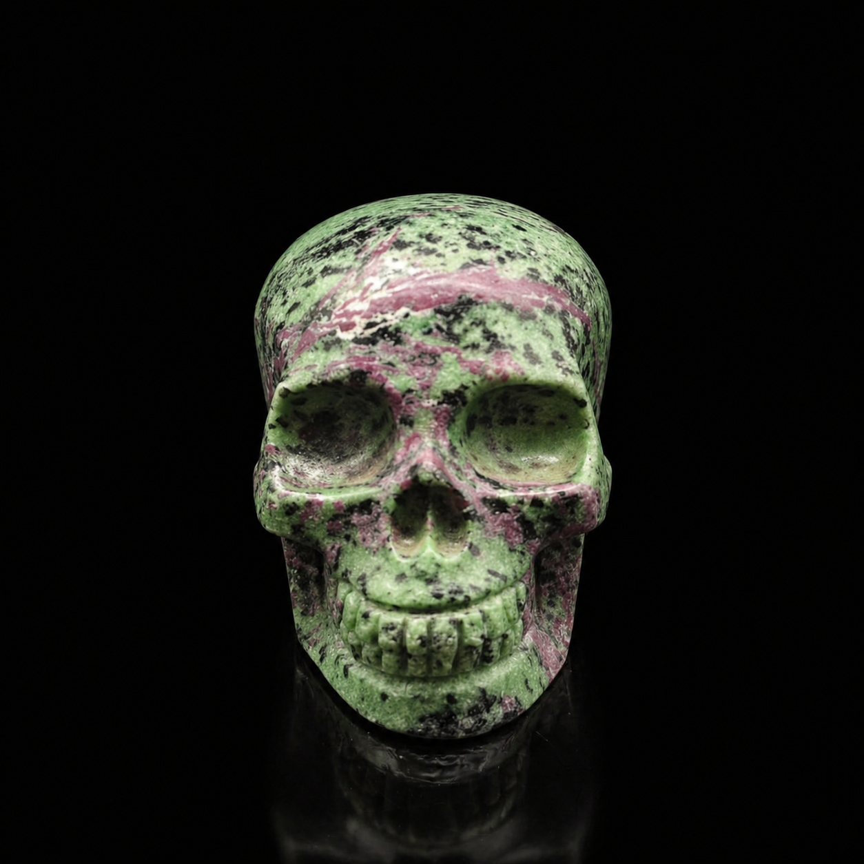 Ruby Zoisite skull front view, 630g polished green crystal carving with ruby-pink veining and dark speckling