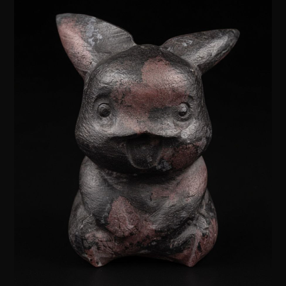Technical frontal photograph of the unique 500g Garnet with Astrophyllite Pikachu carving, showing detailed face, natural bronze Astrophyllite star bursts against dark mineral matrix, on black background