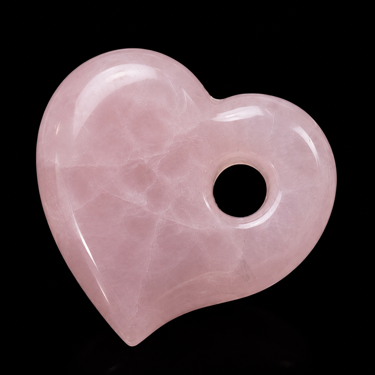 Polished rose quartz heart pendant with drilled hole on black background, showing soft pink colour and natural internal lines