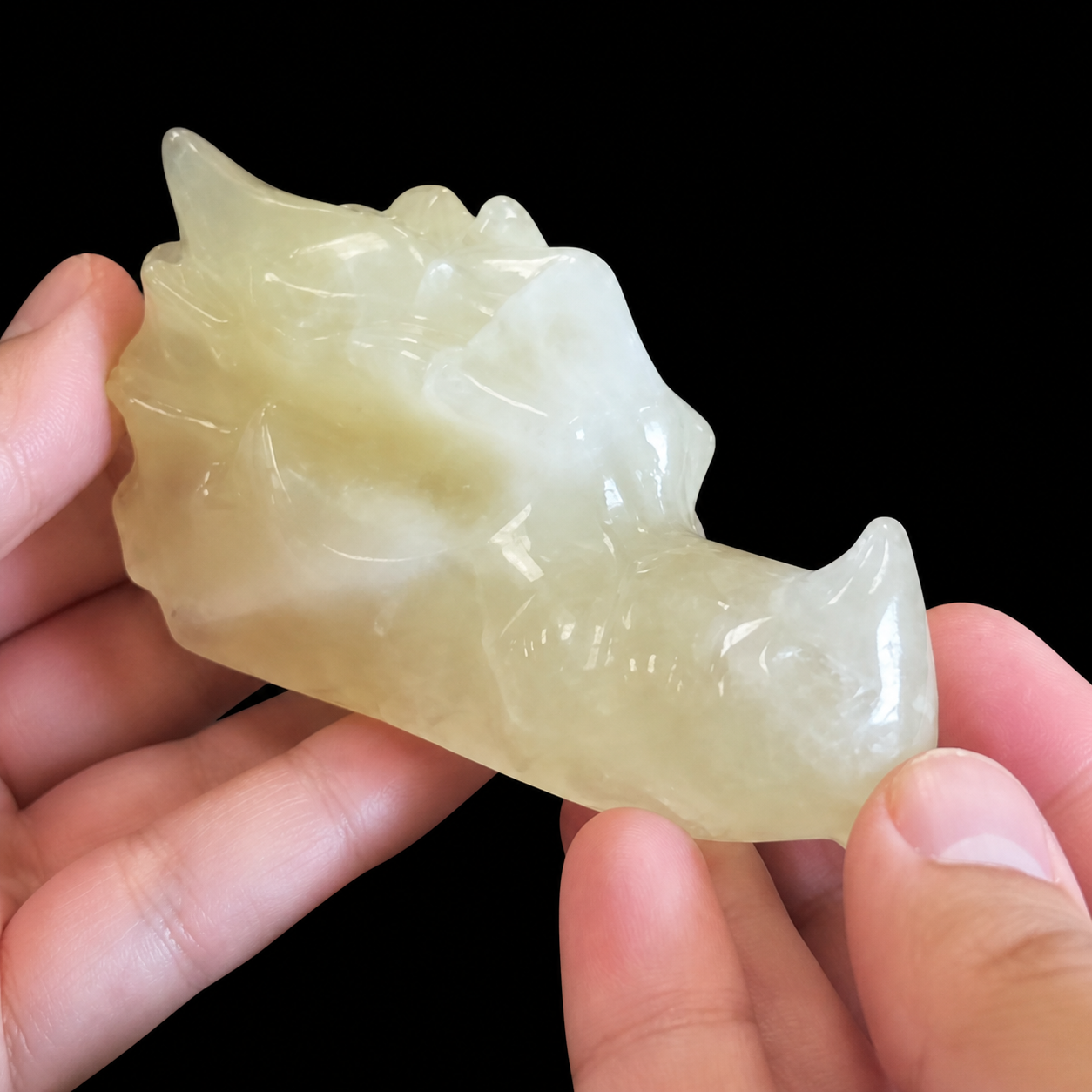 Citrine dragon head carving held in hand, angled front side view showing translucent pale yellow mineral details