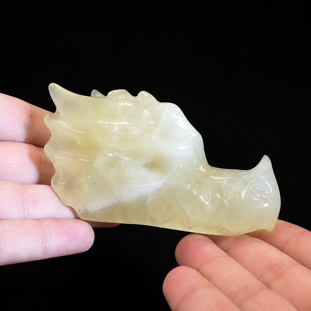 Citrine dragon head carving side view held in hand, showing pale translucent colour and natural cloudy inclusions