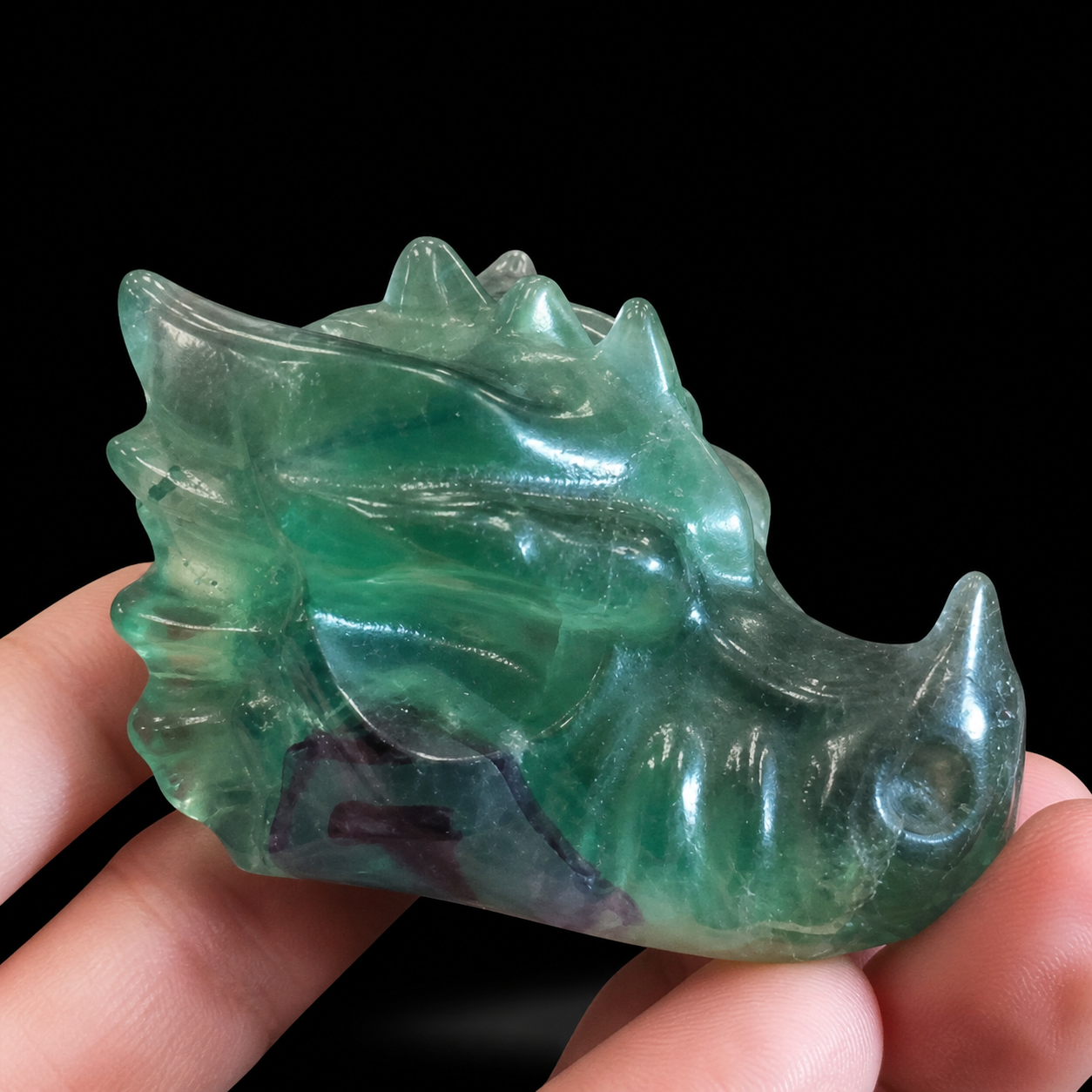 Angled close view of a translucent green fluorite dragon carving showing polished curves and natural inclusions