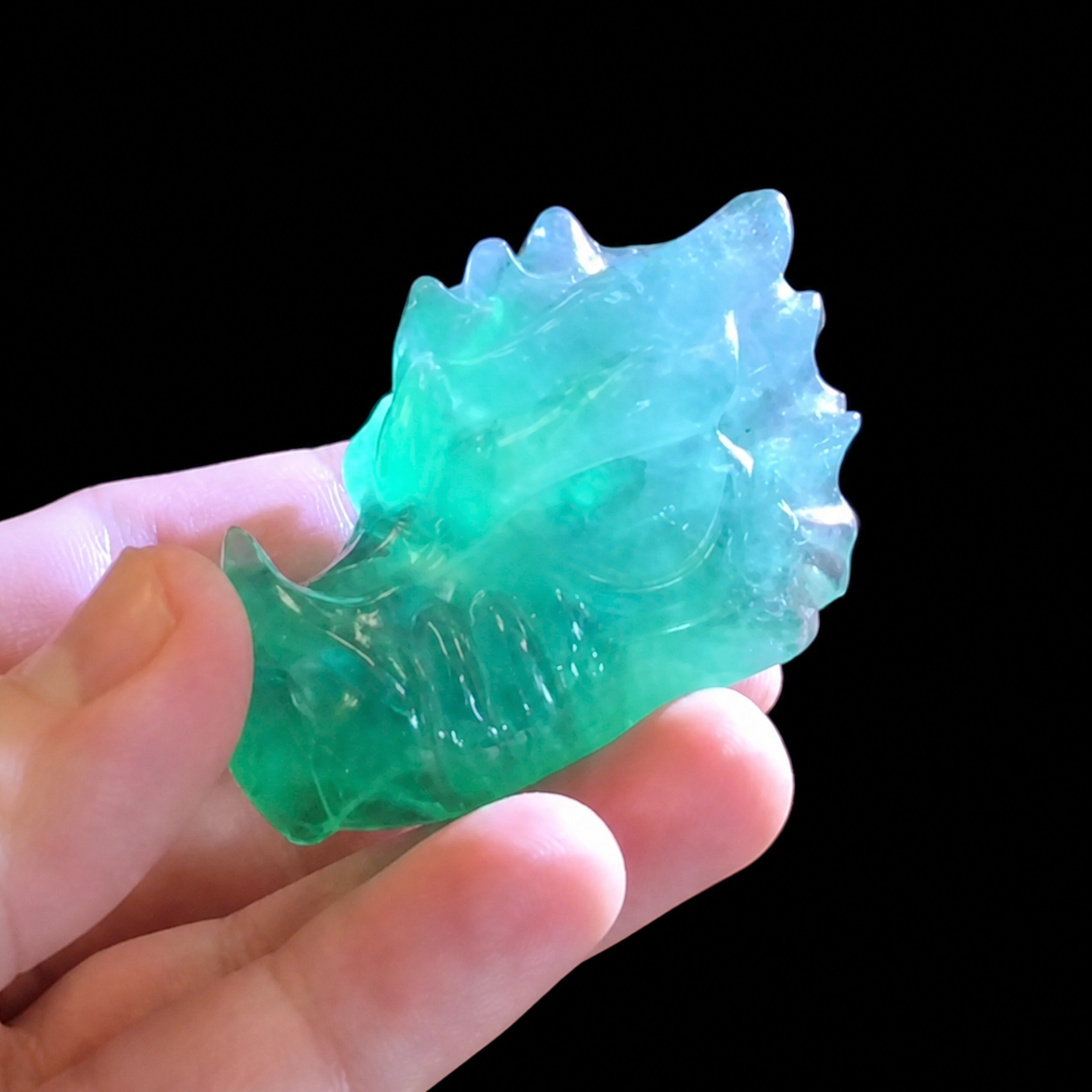 Green fluorite dragon carving illuminated with a torch, showing enhanced translucency and internal colour zoning