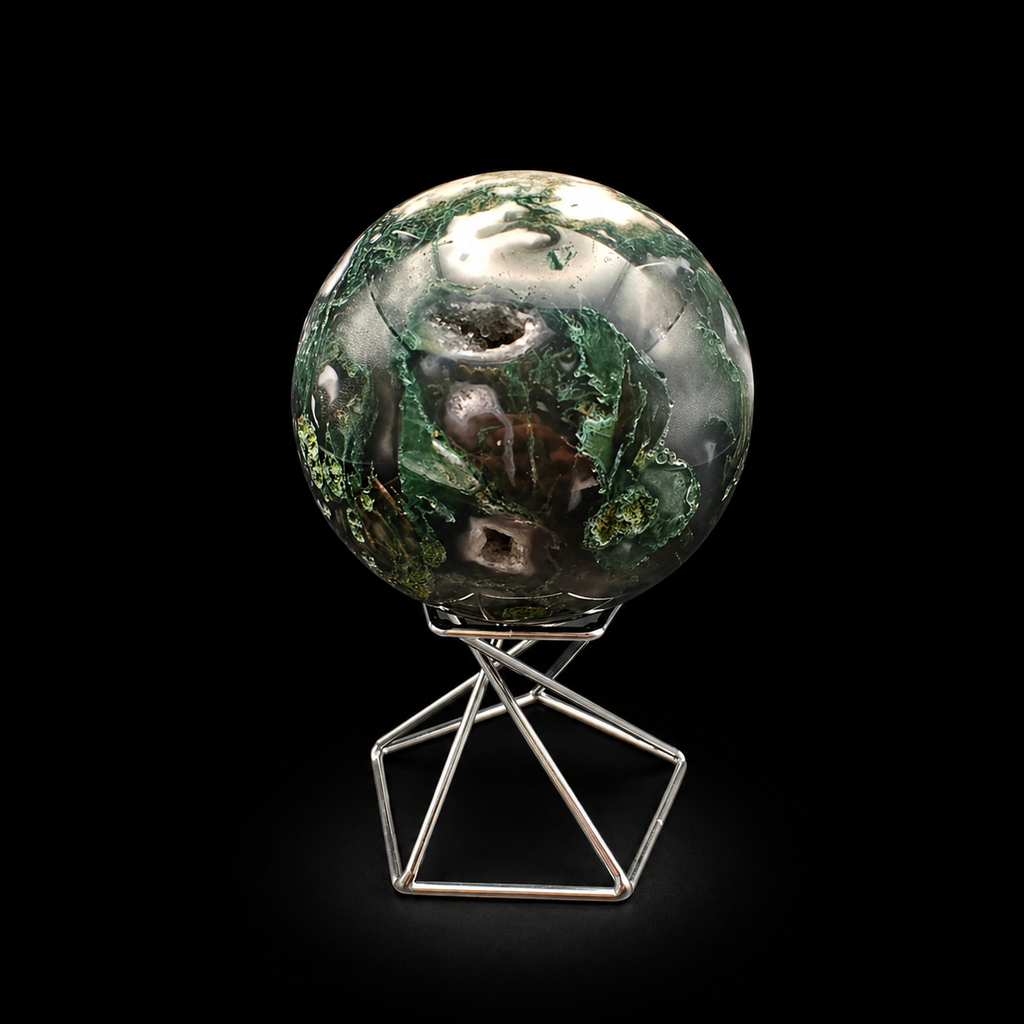 Front view of a polished moss agate sphere 410g with deep green inclusions, natural cavities and creamy white areas on a metal stand