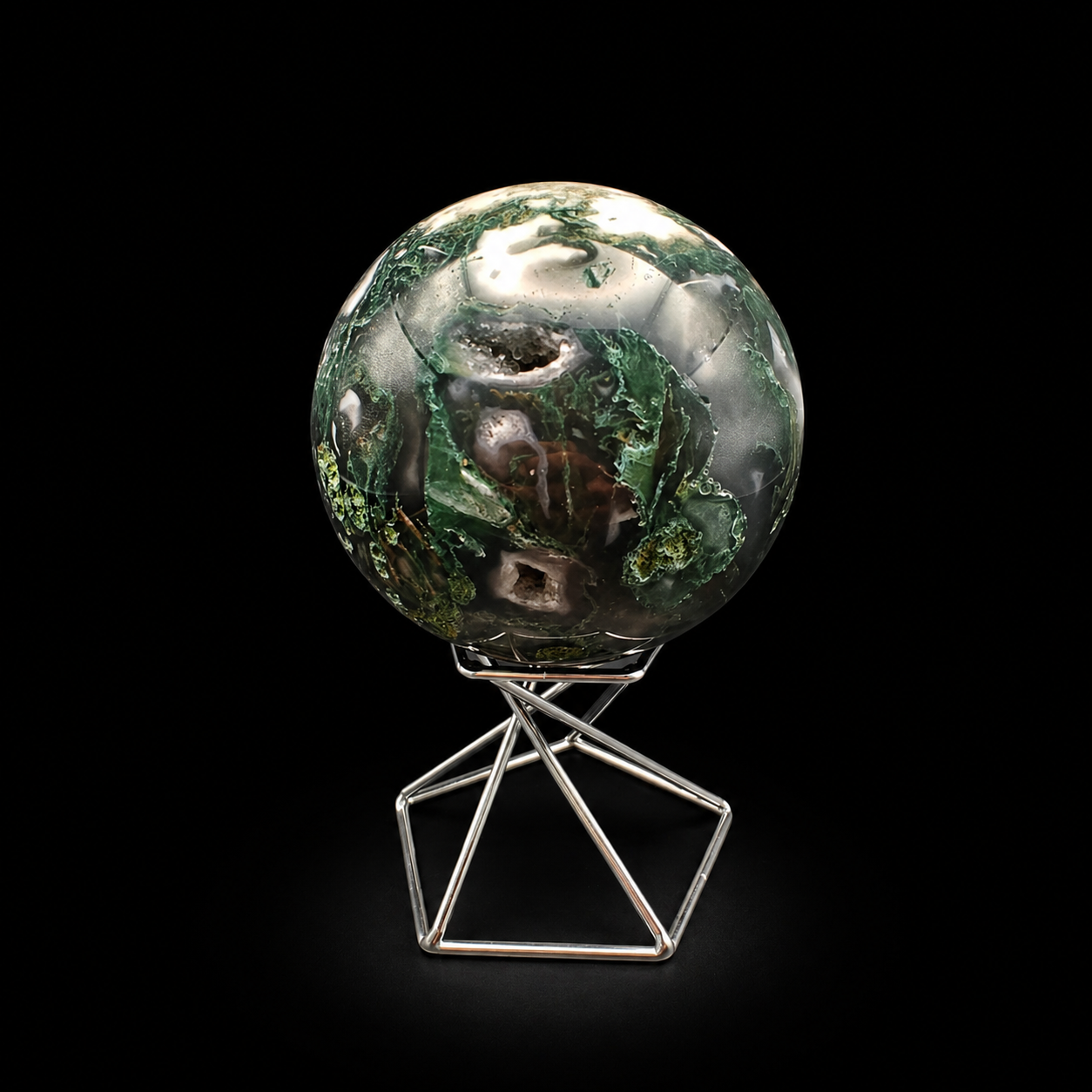 Front view of a polished moss agate sphere 410g with deep green inclusions, natural cavities and creamy white areas on a metal stand
