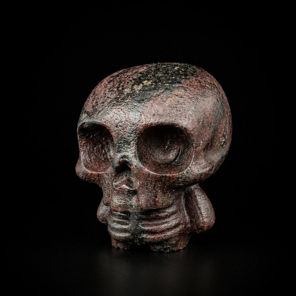 Garnet with astrophyllite skull figure showing deep eye sockets, textured stone surface and metallic flecks, angled front view to the left