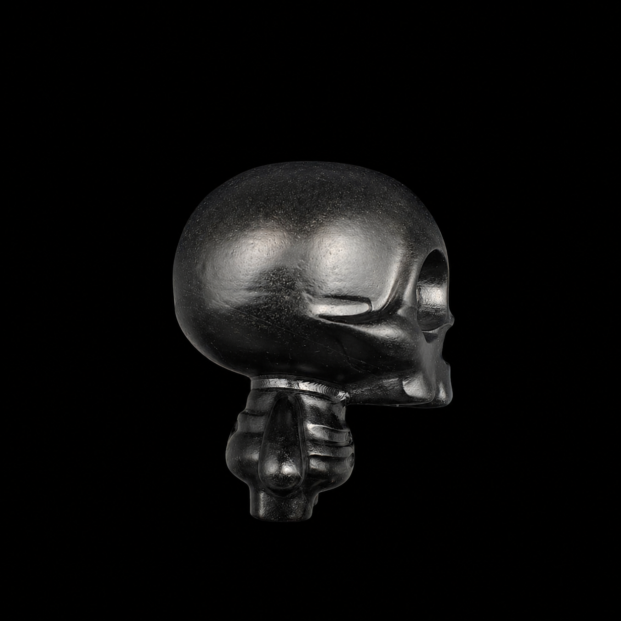 Black obsidian skull carving showing smooth rounded head and polished black volcanic glass, side view