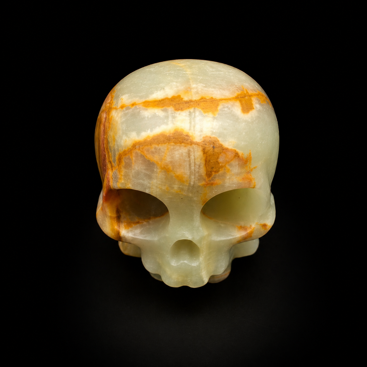 Green banded onyx skull carving showing large eye sockets, pale green onyx and orange veining, front view