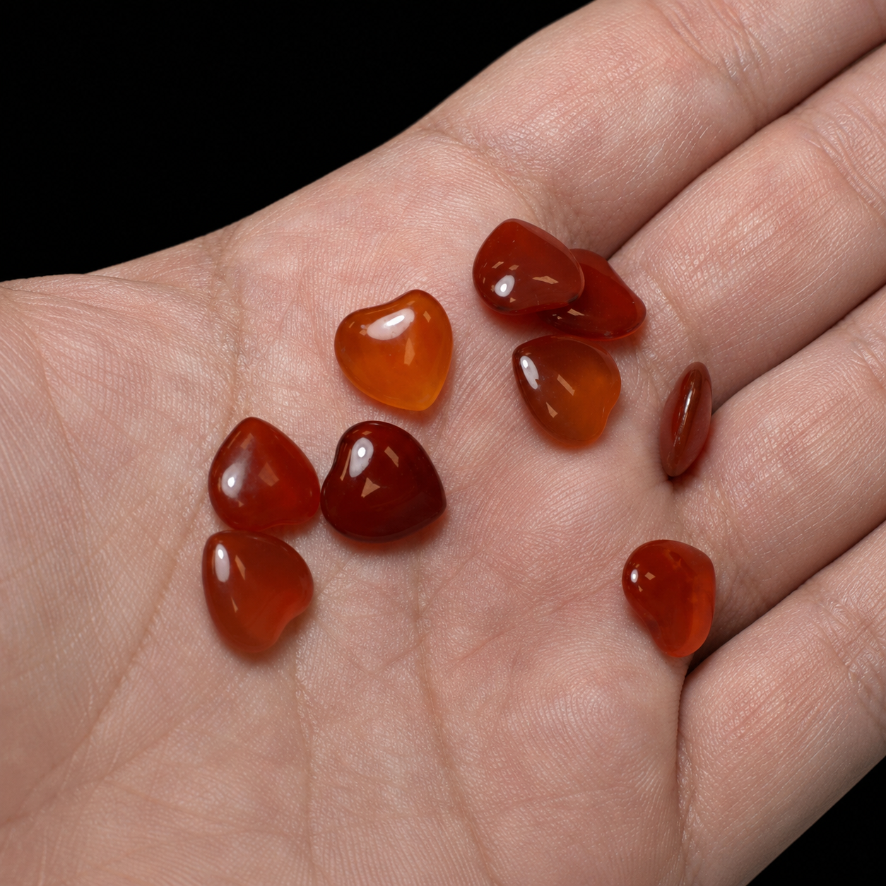 Mini polished carnelian heart stones on a hand, close-up view showing translucent orange-red colour, glossy finish and size reference