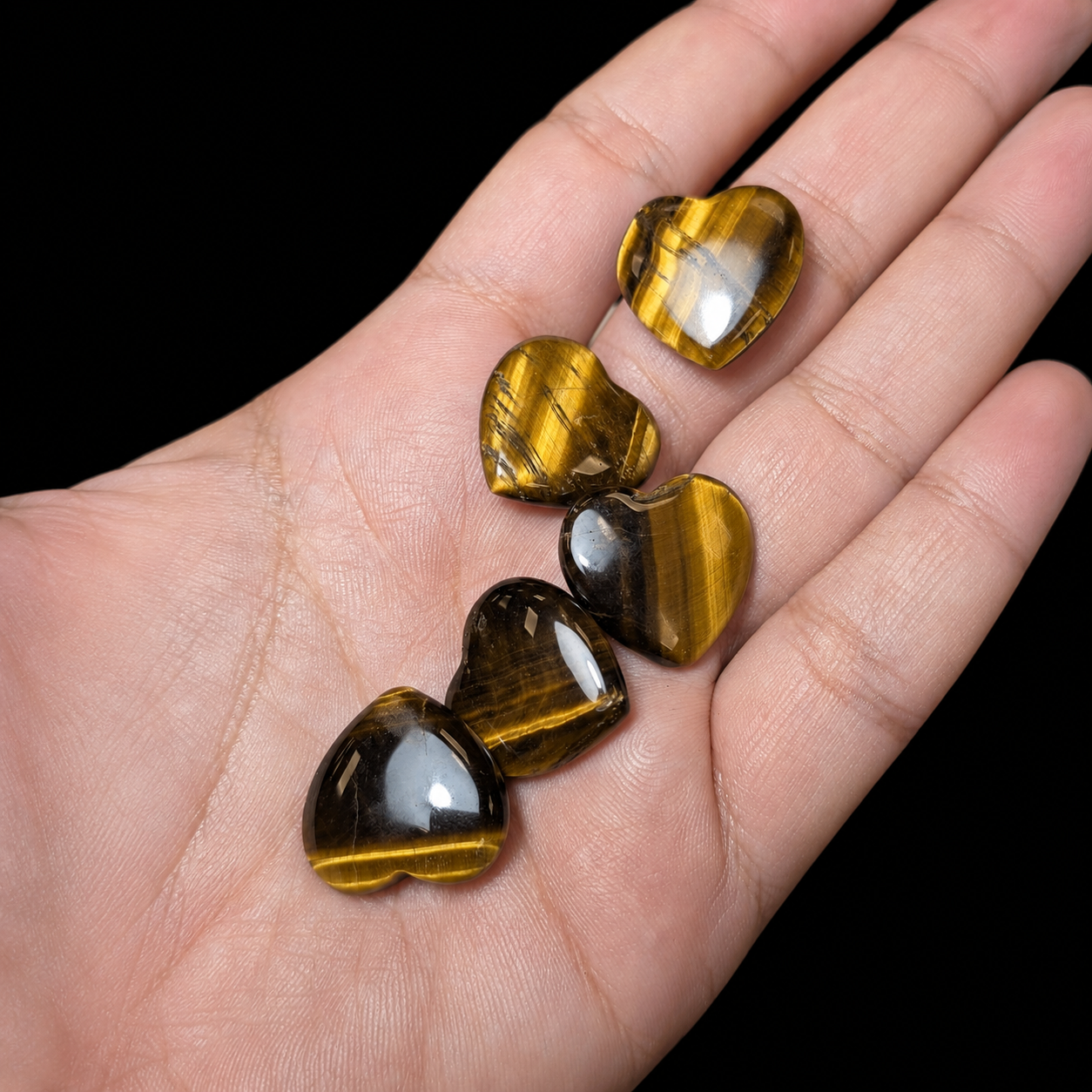 Small polished Tiger’s Eye heart stones displayed on a hand, close-up view showing golden brown chatoyancy, glossy finish and size reference