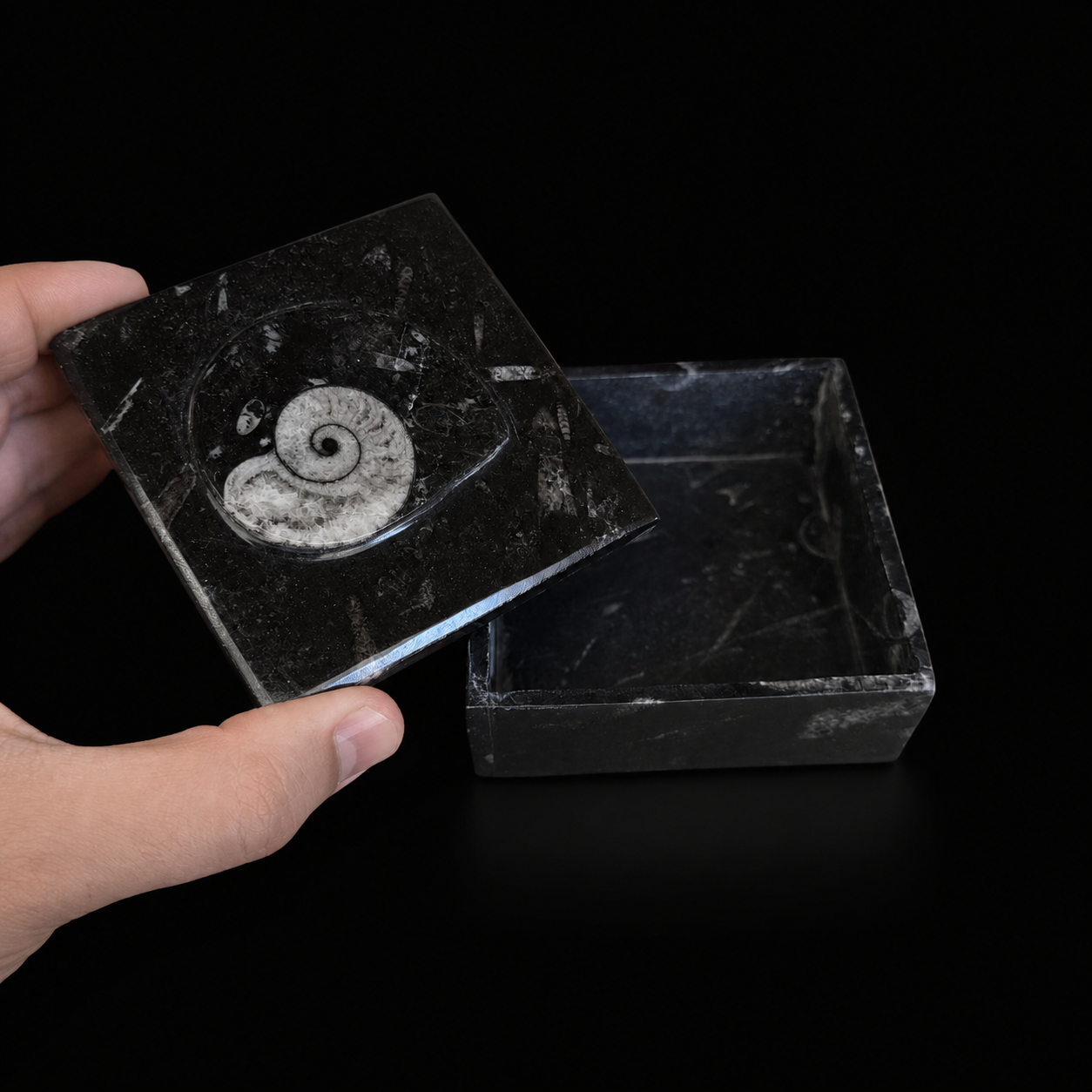 Open square fossil jasper jewellery box with lid held by hand showing the interior