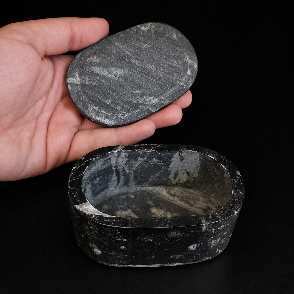 Open oval fossil jasper jewellery box with lid held by hand for size reference