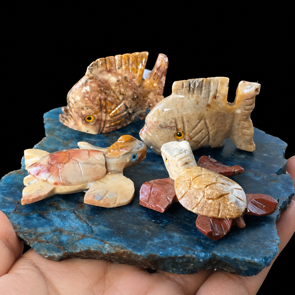 Apatite and steatite marine animal carving lot with two fish and two turtles on a blue Madagascar apatite base, held in hand for size reference