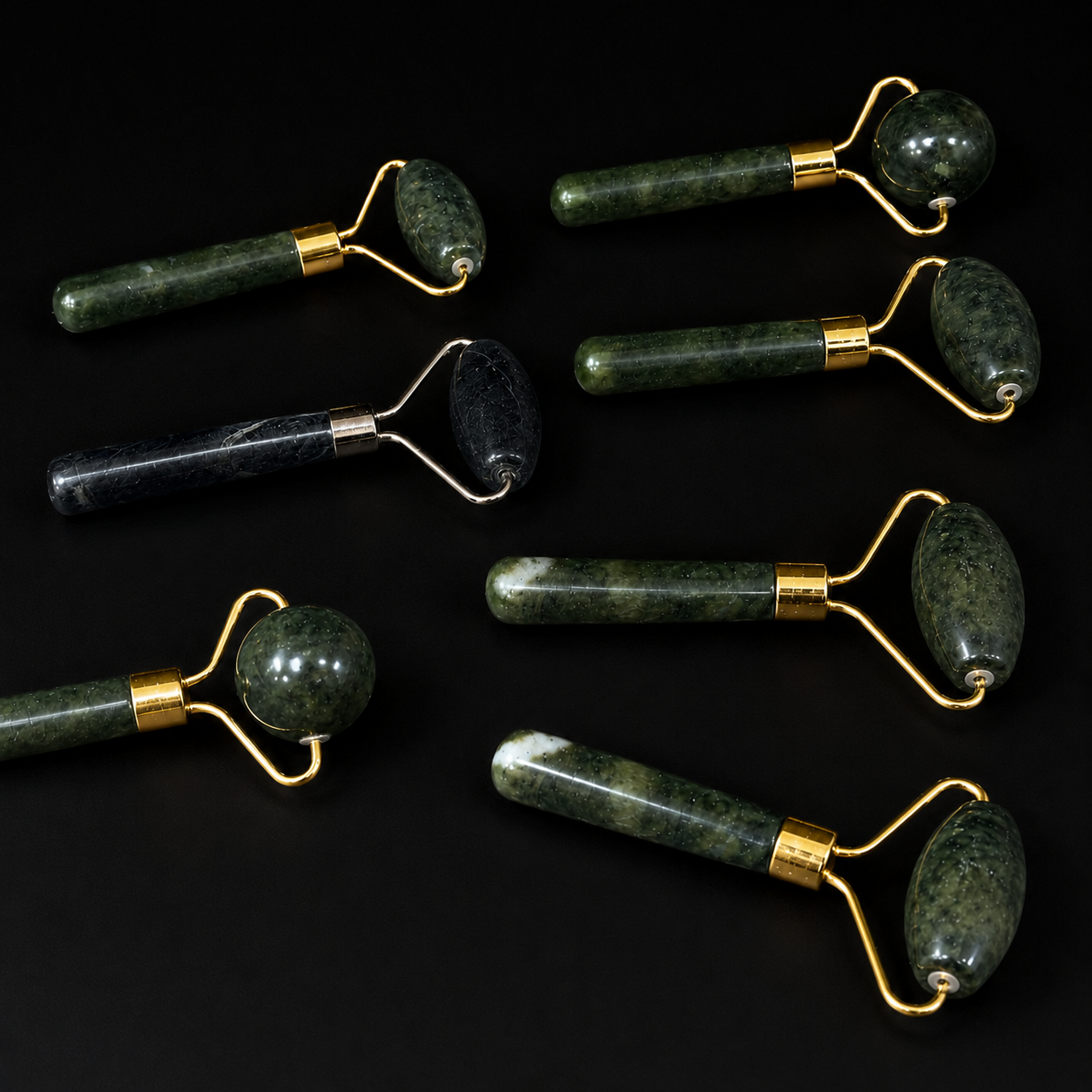 Assorted jade and black onyx facial massage rollers with spherical and elongated roller heads displayed on a black background.
