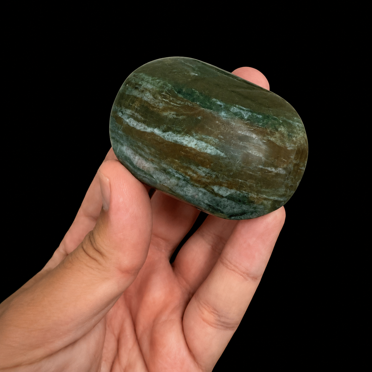 Ocean Jasper XL palm stone held between fingers, angled side view, polished green jasper soap stone with soft blue-green banding and earthy brown streaks | HeyMiner