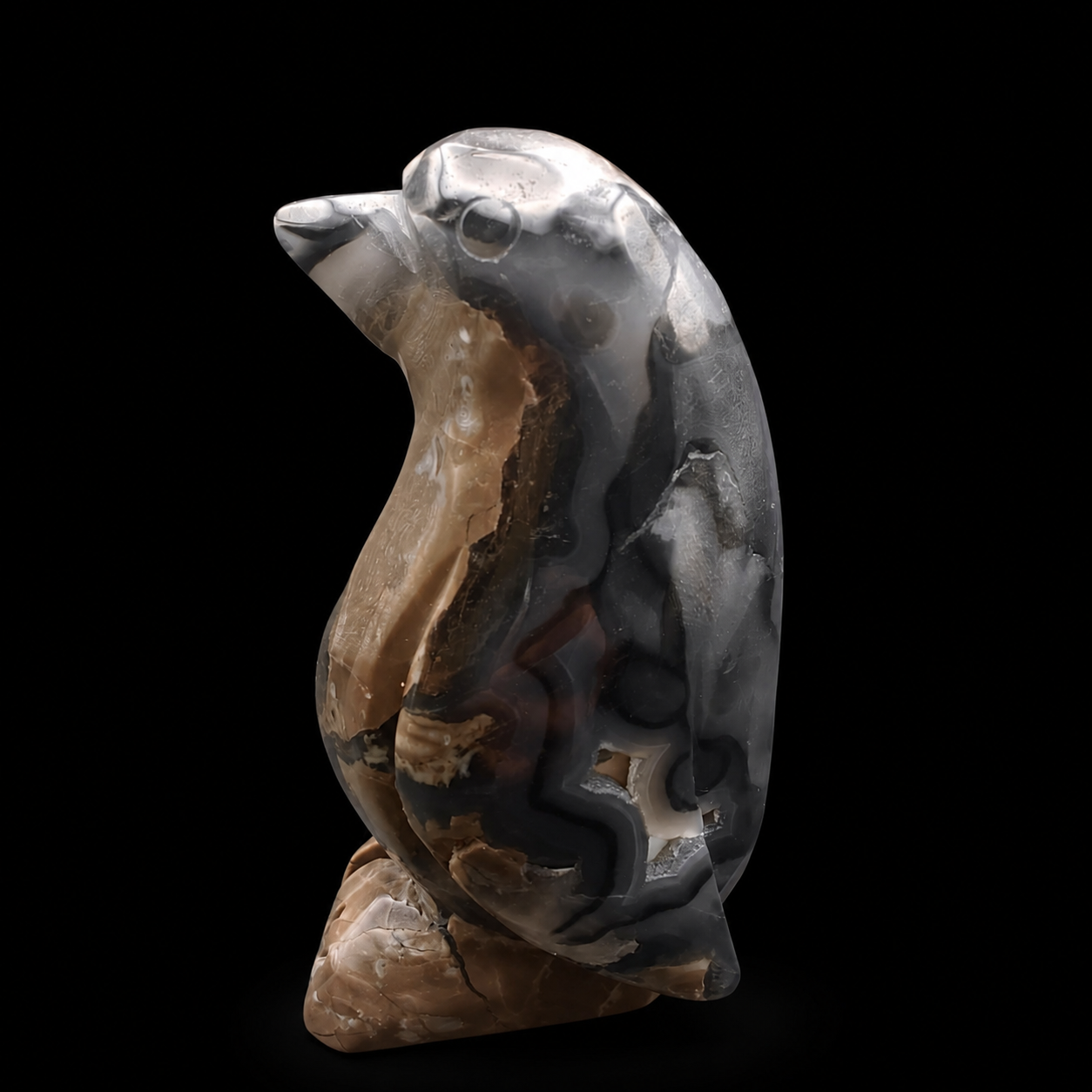 Left side view of a UV reactive volcanic agate penguin carving 465g showing dark grey and brown agate patterns