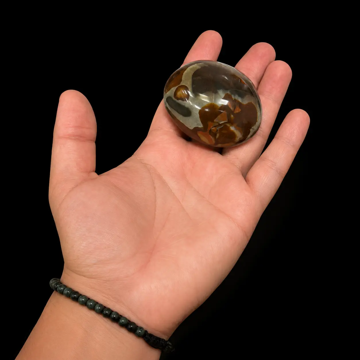 Medium polychrome jasper palm stone held in hand, featuring brown, cream and smoky grey natural patterns on a black background.