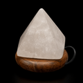 Angled front view of a white quartz 7 chakras LED lamp on a rounded wooden base, showing its translucent mineral texture and power cable.