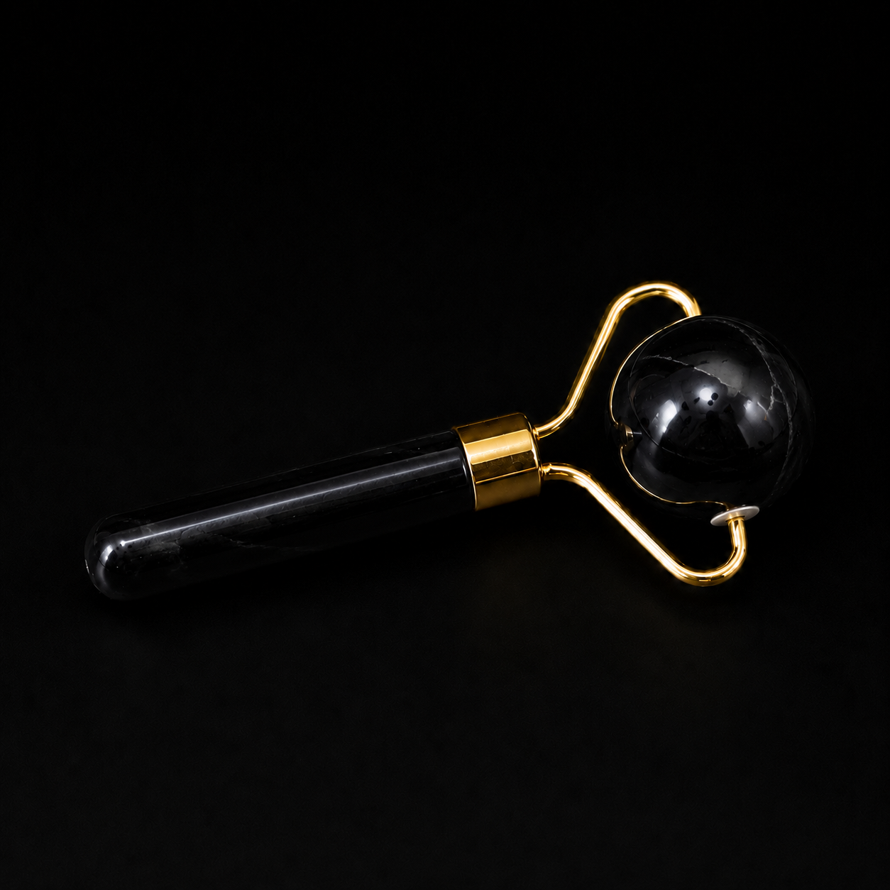 Black onyx facial massage roller with spherical roller head and gold-tone fittings on a black background.